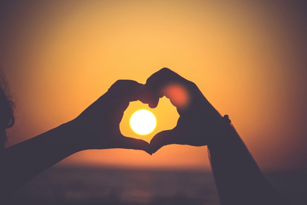 two hands form a heart around a setting sun