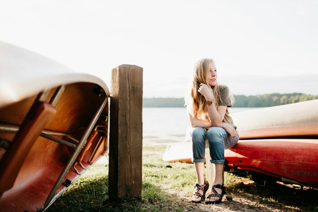 a white woman sits outside in front of a canoe