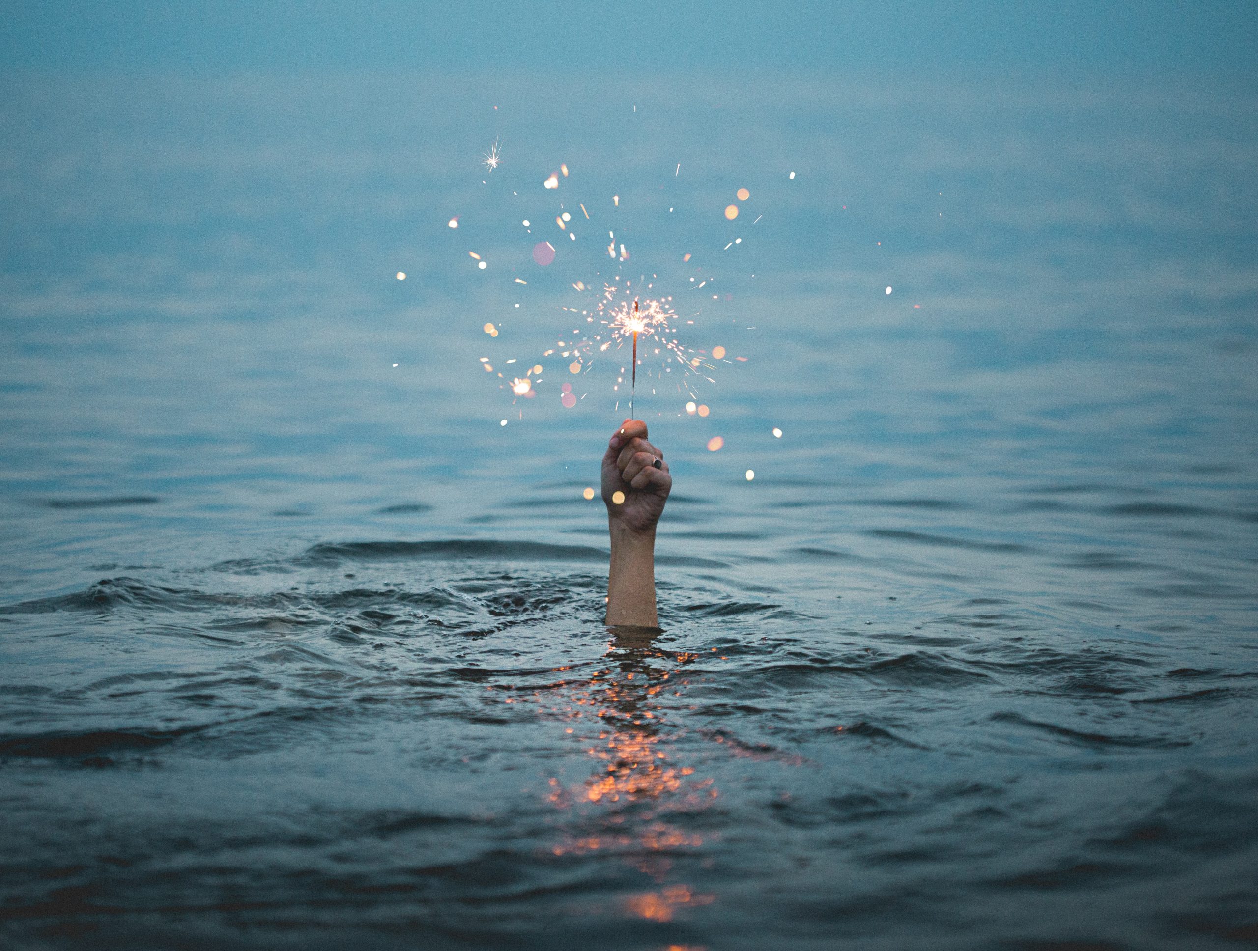 a hand holding a sparkler plunges out from the water